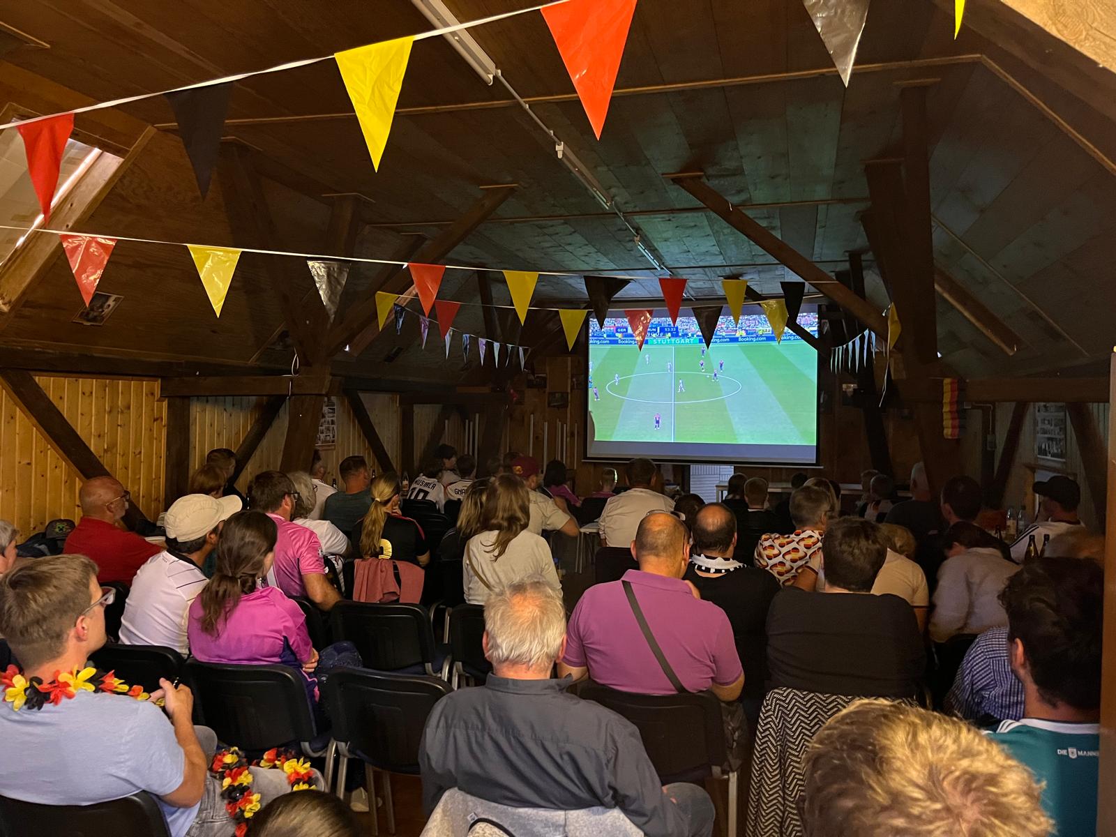 Blick in das Obergeschoss der Eigenheimerhalle in Waigolshausen während des Public Viewing. Voll besetzt mit Deutschlandfähnchen als Dekoration. Blick auf die Leinwand, die das Fußballspiel zeigt.