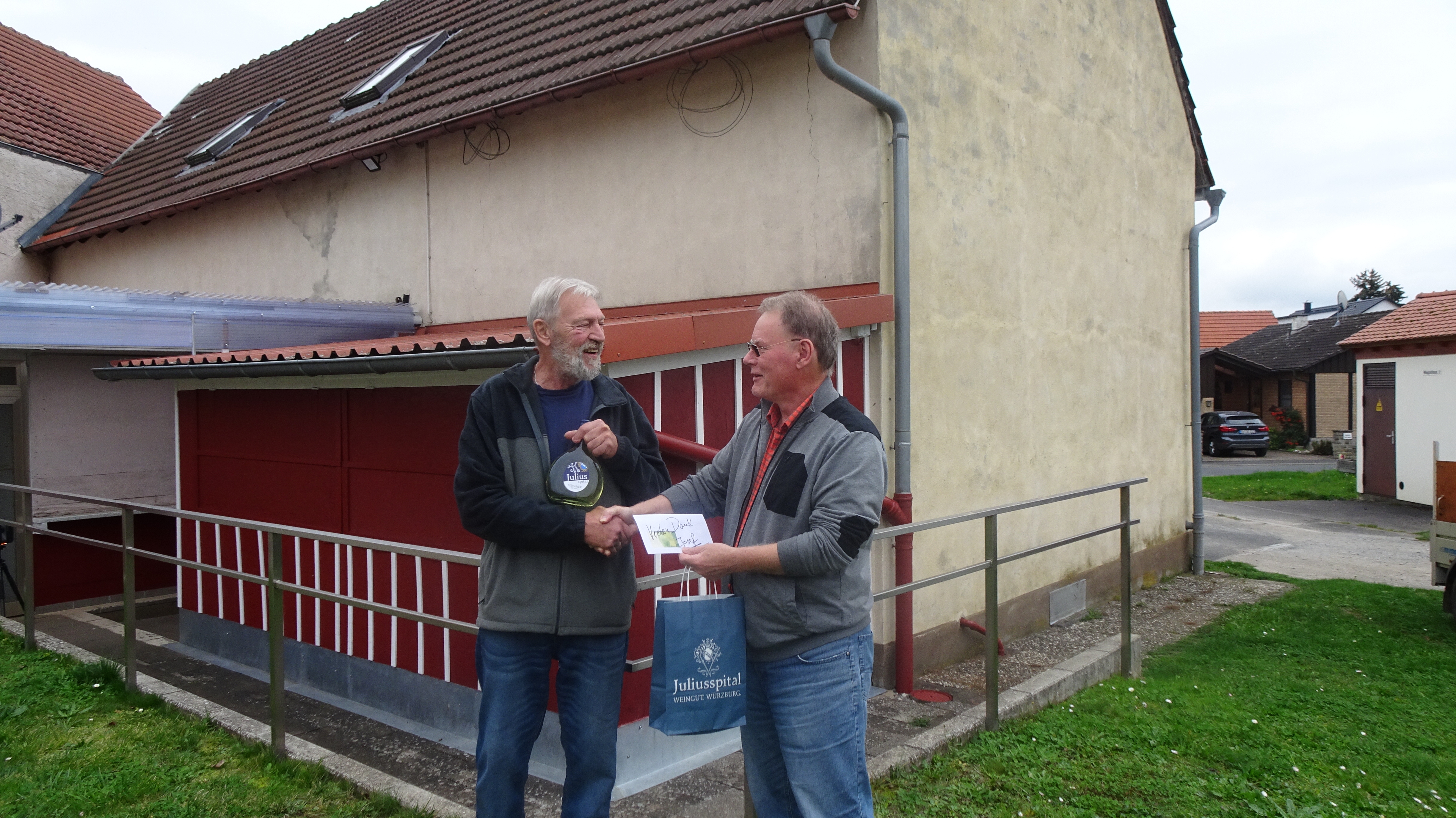 Vorstand Helmut Werthmann überreicht Josef Müller aus Waigolshausen einen Bocksbeutel. Im Hintergrund die neu gestrichenen Hütten.